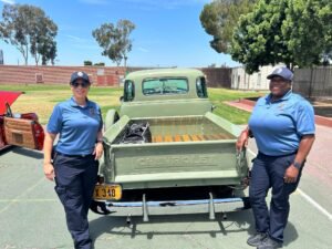 two female probation officers standing behind a classic truck