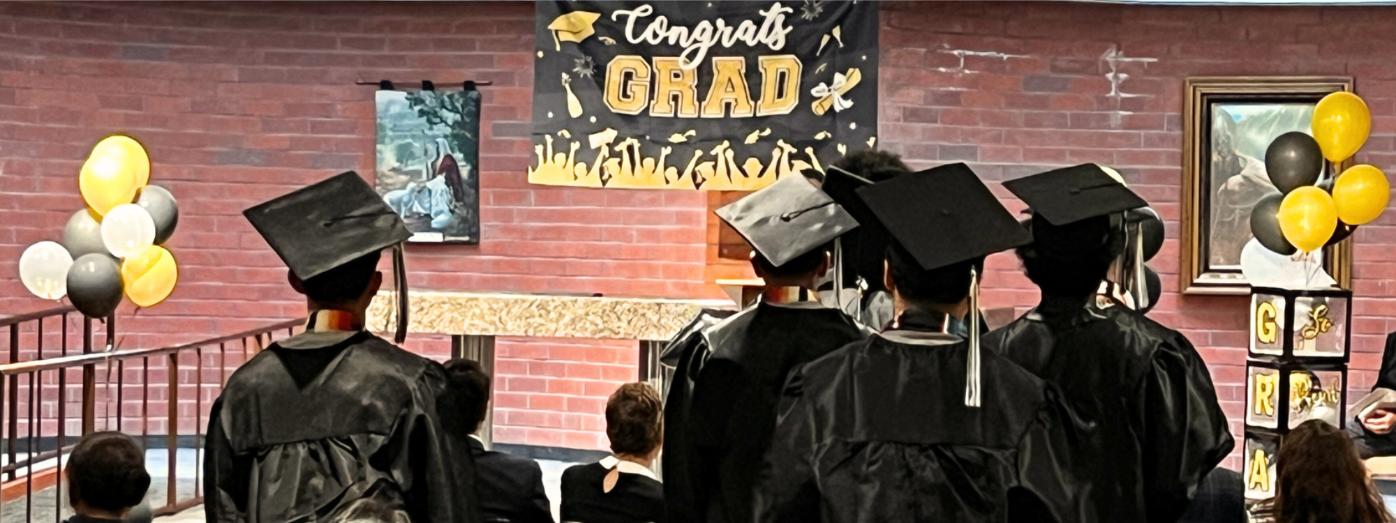 Picture of graduates in cap and gown from the back and congrats banner hanging on wall